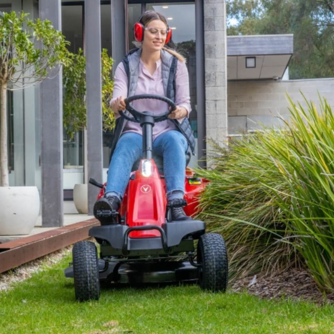 Woman carefully steering her ride on mower around a garden bed.