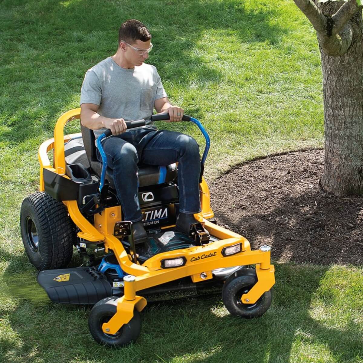 Man driving his yellow ride on mower around a tree with his zero turn steering via lap bars.