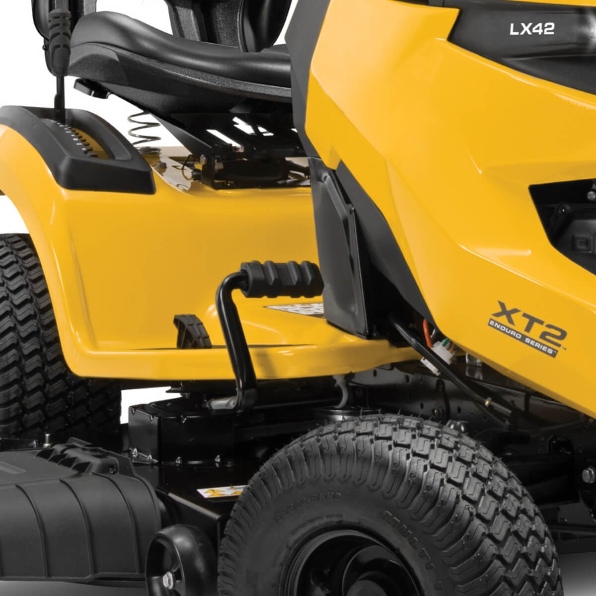 Close up view of a ride on mower showing tread on tires, foot pedal, cutting height lever and suspensioned seat.
