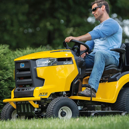 Man operating a yellow Cub Cadet XT2 LX46 lawn mower in a grassy area with trees in the background.