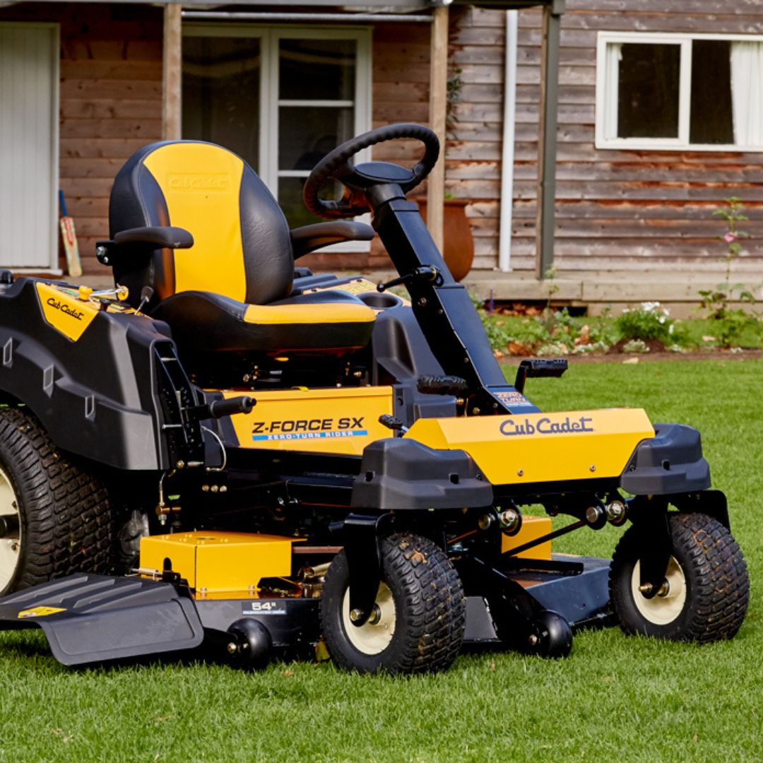 Yellow and black Z Force SX Cub Cadet ride on lawn mower on a grassy area with a wooden building in the background.