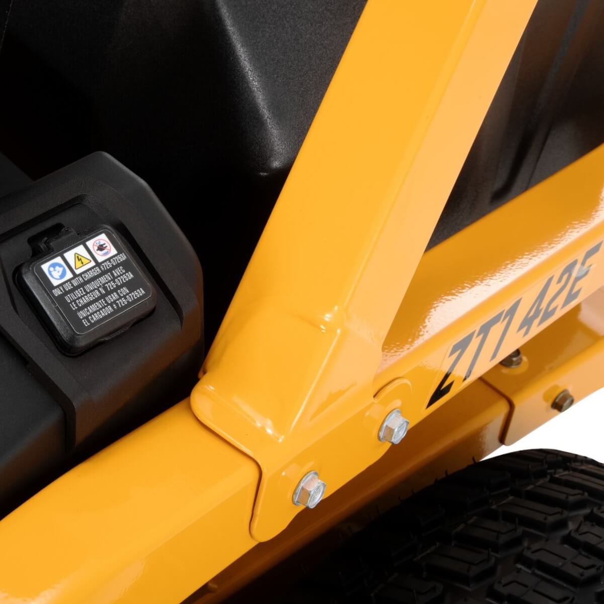 Close-up of a yellow ride on mower ZT1 42E Cub Cadet side frame with a charging point and treaded tire.