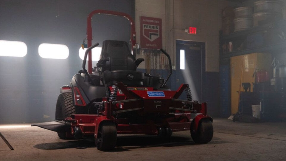 A red Ferris 300S zero turn ride on mower parked in a dark garage with bright lighting shining through the windows of the roller door.