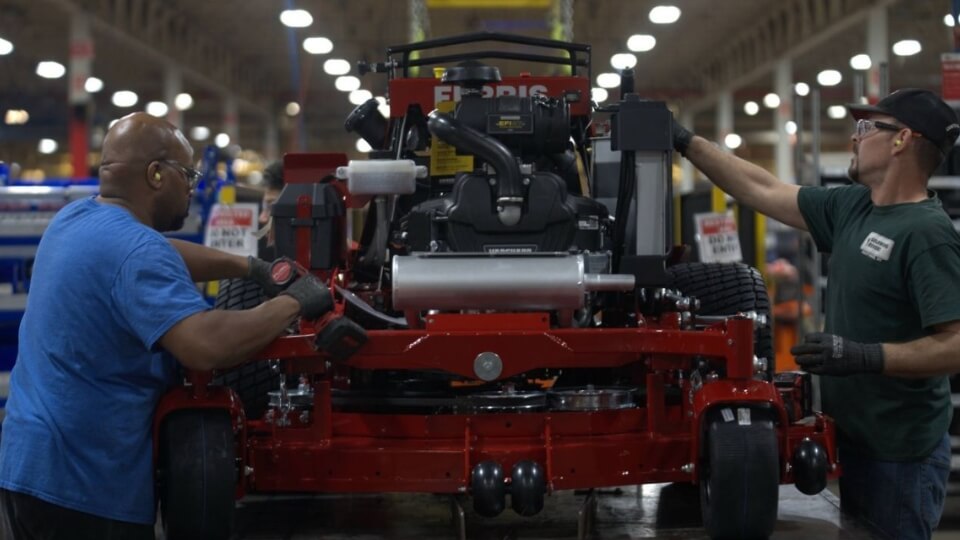 Two men on a product line in a ride on mower factory, building the Ferris red 300S.