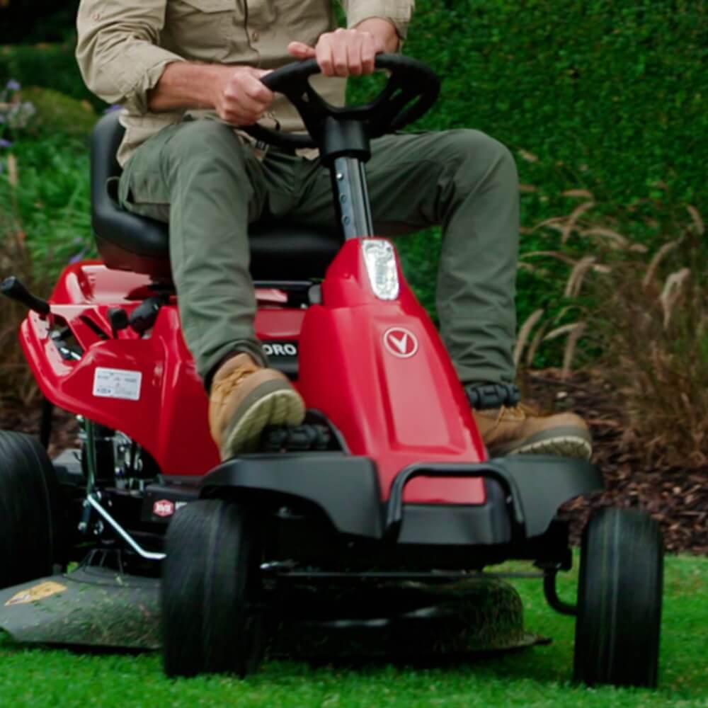 Person operating a red riding lawn mower on grass.