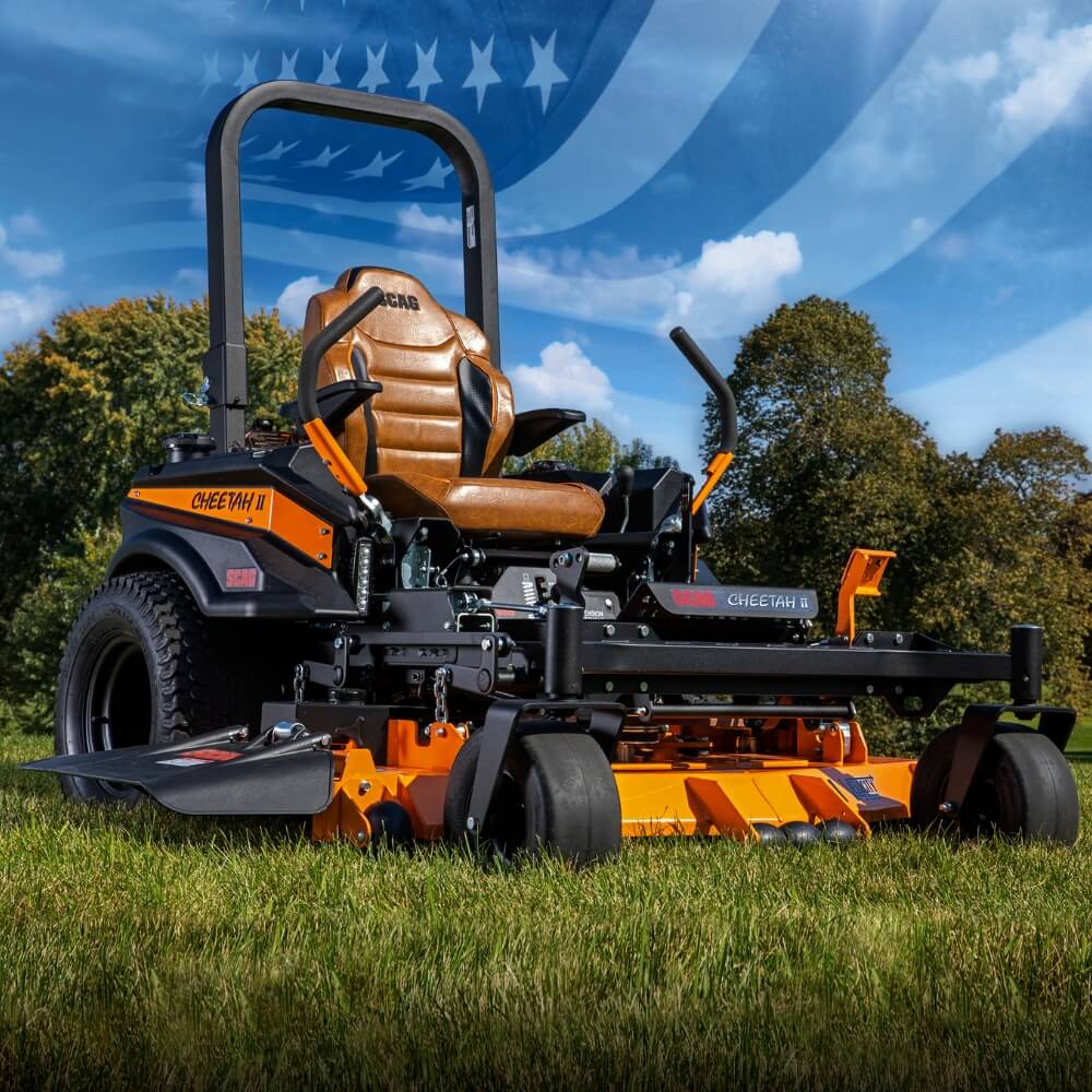 Orange and black SCAG Cheetah riding lawn mower on grass with a blue sky and trees in the background