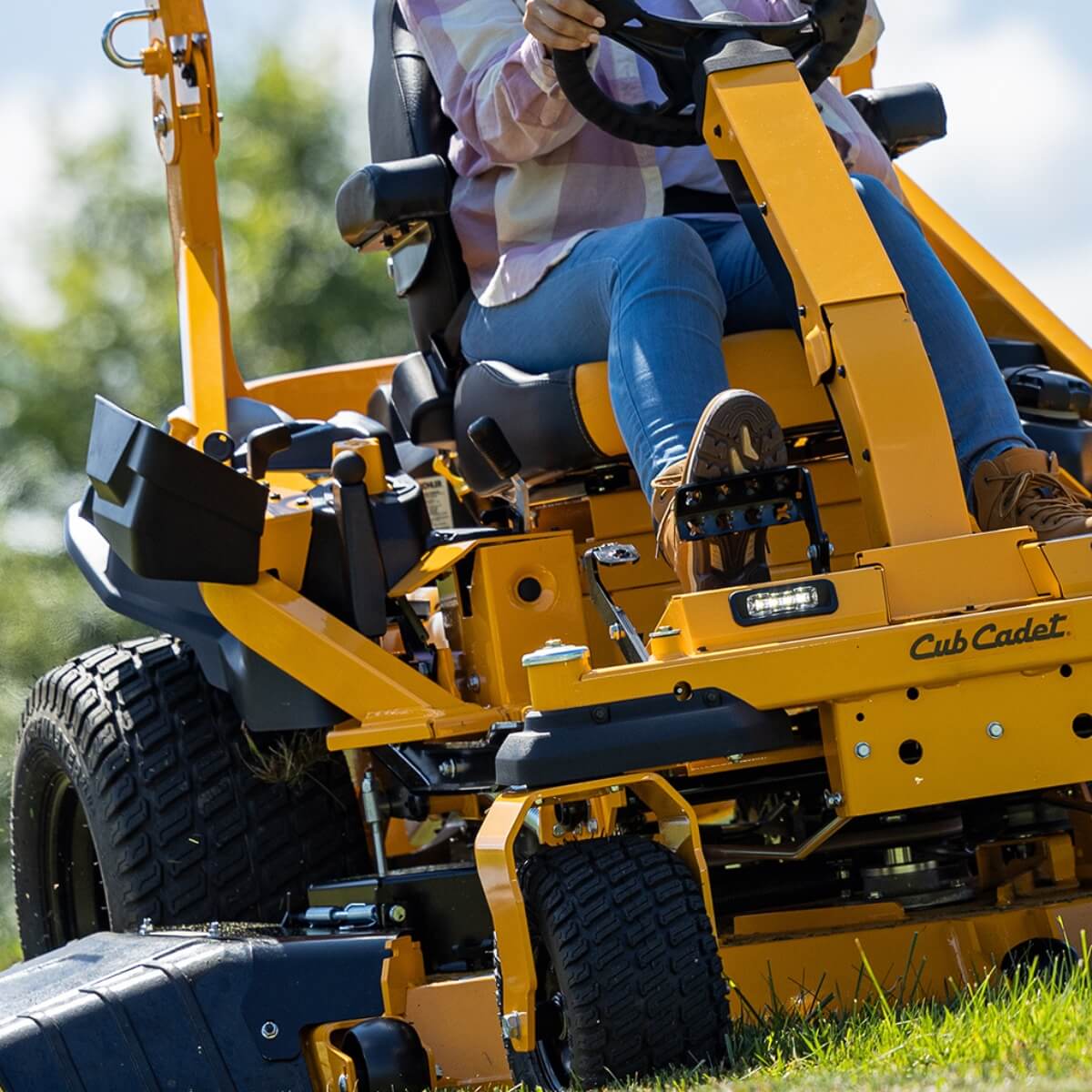 Woman wearing jeans driving her ride on mower with steering wheel and foot pedal.