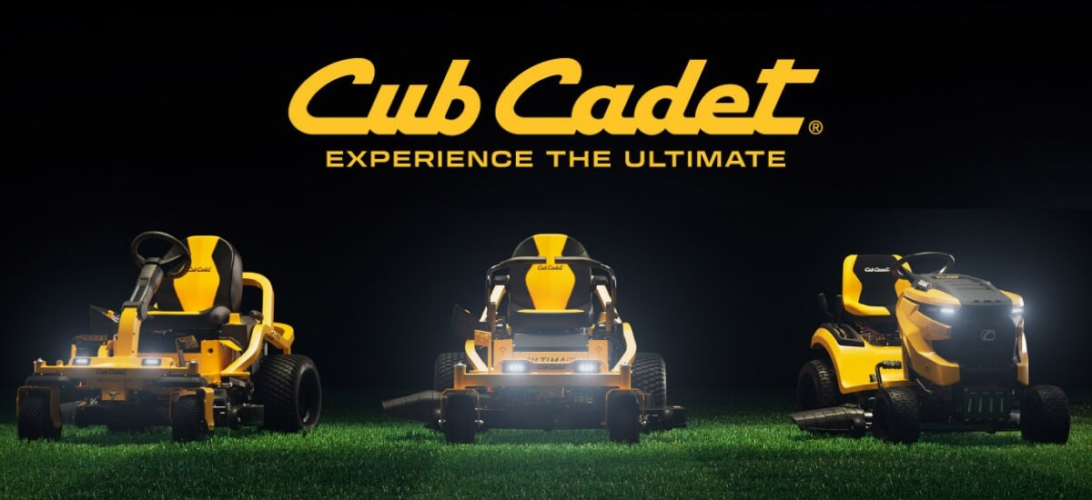 Large Cub Cadet logo with three yellow ride on mowers sitting on green lawn with lights on with black background.