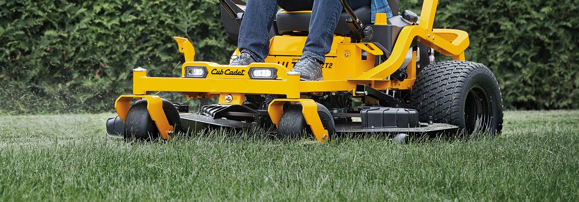 Person operating a yellow Cub Cadet lawn mower on grass