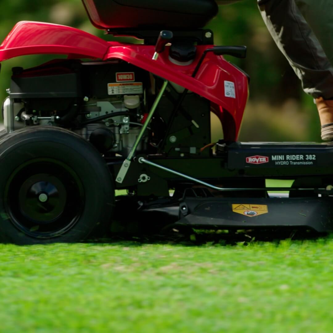 Close up side and low view of a person operating a red Rover ride on mower.