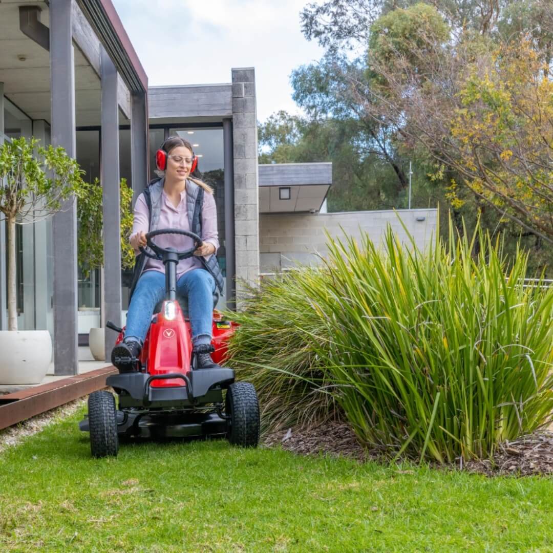Person using a red riding lawnmower in a garden setting