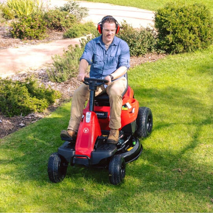 Man operating a red riding lawn mower on a grassy area with headphones on.
