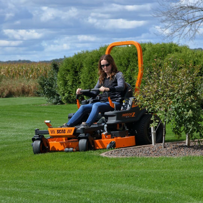 Person operating a SCAG lawn mower on a grassy field with trees in the background