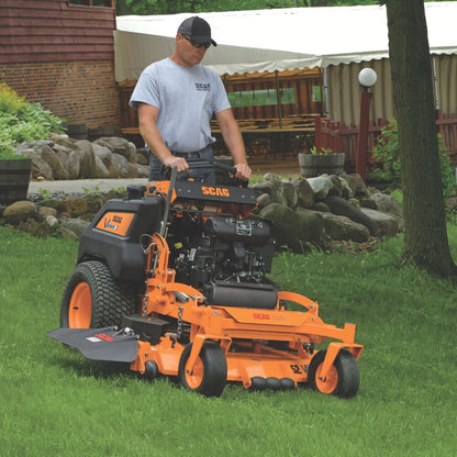 Man operating a large orange SCAG lawn mower in a backyard setting.