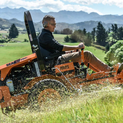 Person operating a SCAG mower in a grassy field in New Zealand with mountains in the background