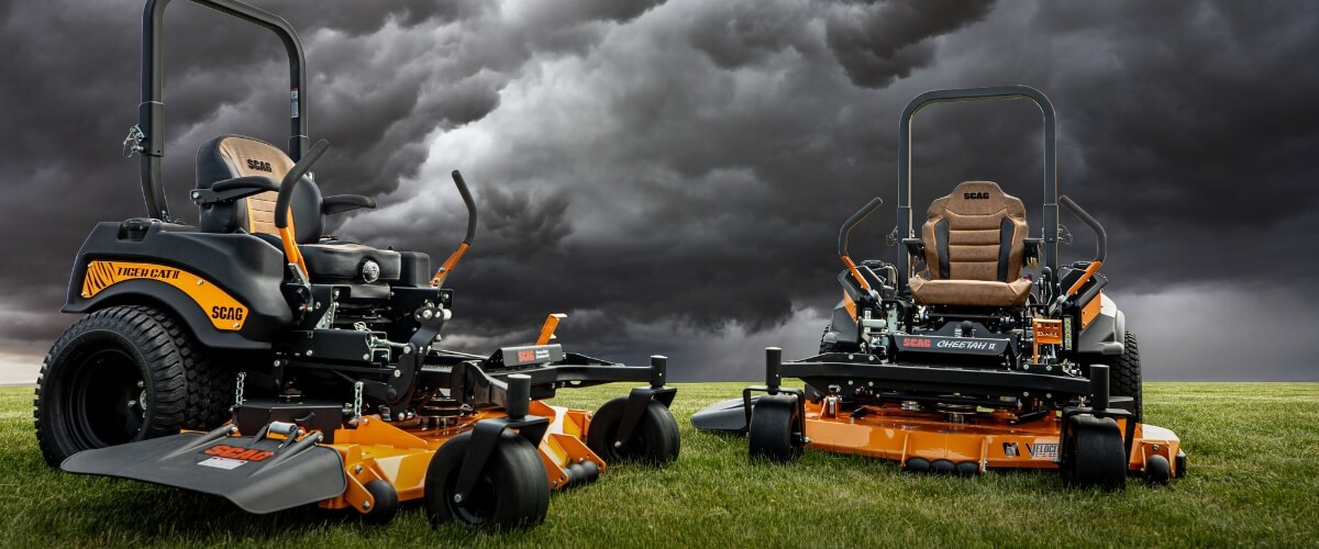 Black and range SCAG ride on mowers sitting on green lawn with dark grey clouds on the horizon.