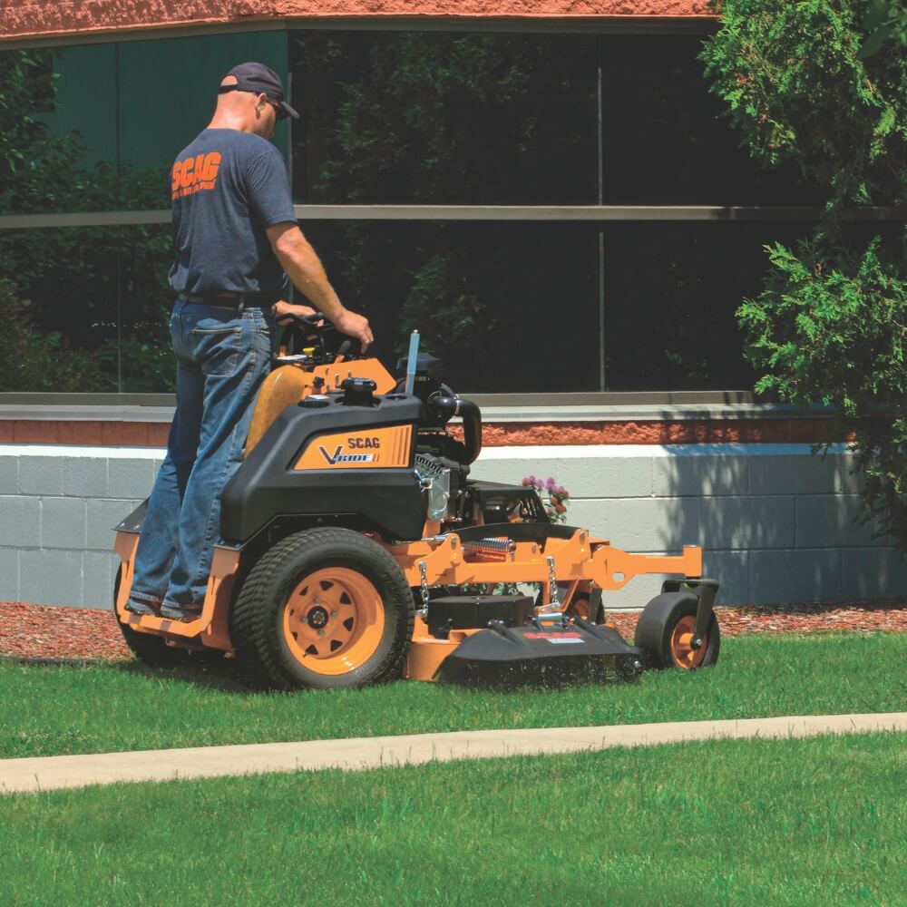 Man operating a riding lawn mower on grass with a building in the background