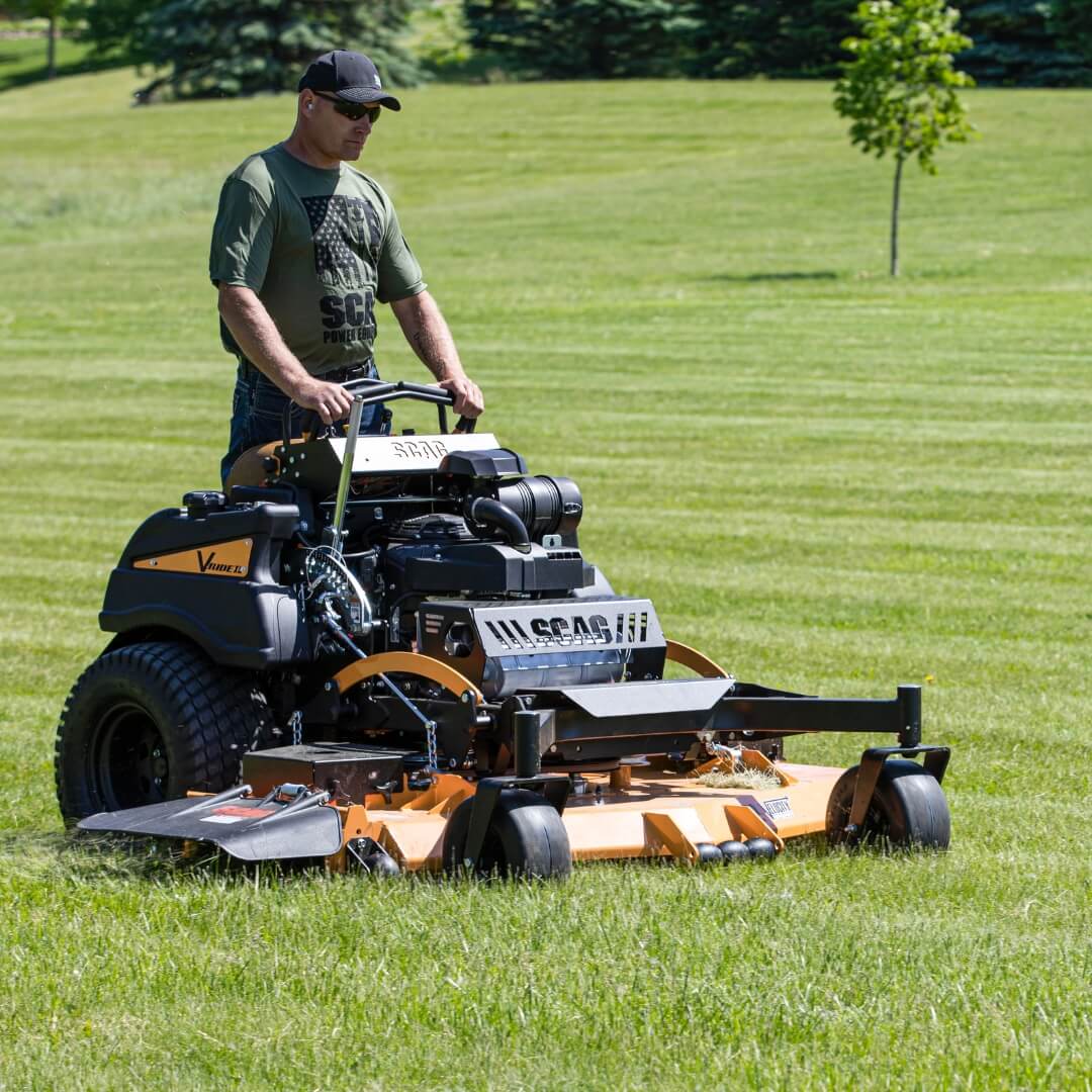 Man standing and operating his mower cutting long green grass.
