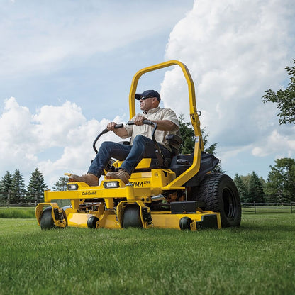 Man operating a yellow riding lawn mower on a grassy field with trees and blue sky in the background.